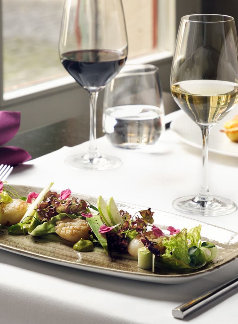 Gedeckter Tisch mit Weingläsern und Gourmetgemüse auf einem Teller.