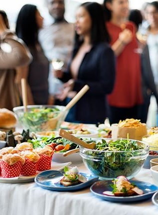Buffettisch mit verschiedenen Speisen, Menschen im Hintergrund stehend.