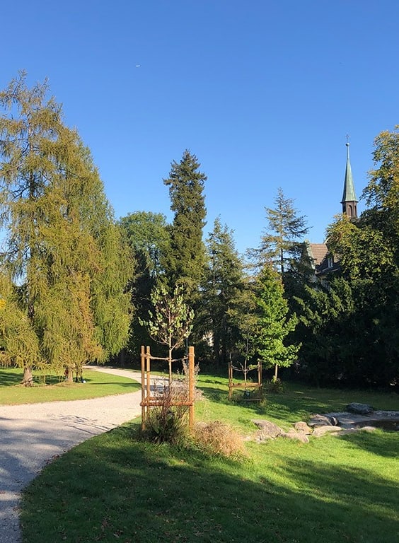 Parklandschaft mit Kirche im Hintergrund unter blauem Himmel.
