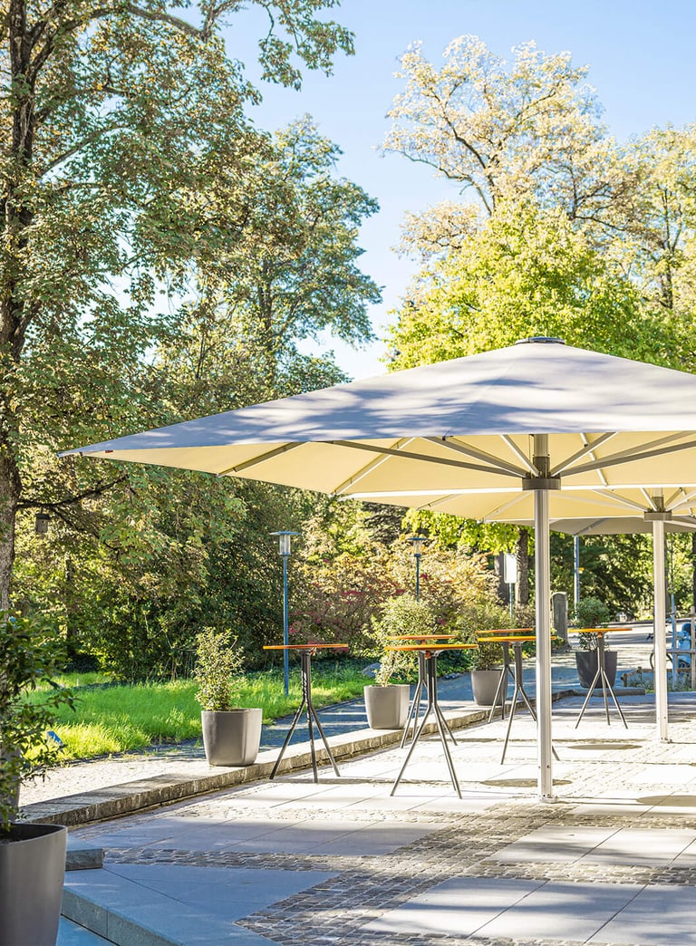 Terrasse mit Sonnenschirmen und Bäumen im Hintergrund.