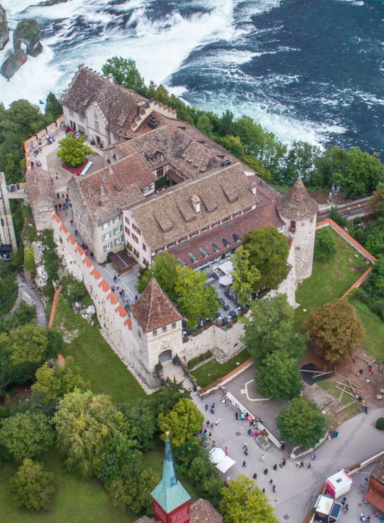Luftbild eines Schlosses am Fluss mit Wasserfällen und einer Brücke.