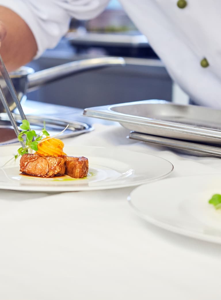 Koch richtet Gourmetgericht mit Pinzette an.