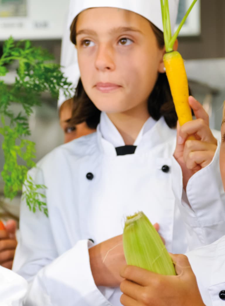 Kinder in Kochuniformen halten Gemüse hoch."  