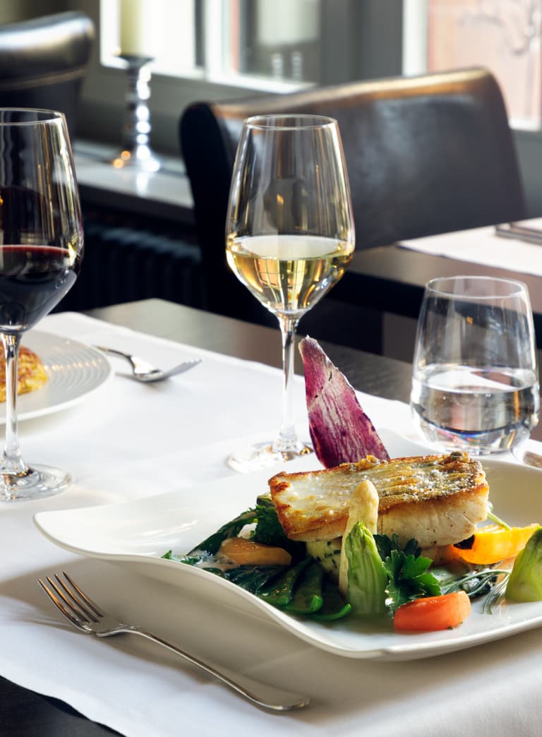 Gedeckter Tisch mit zwei Weingläsern und Teller mit Essen.