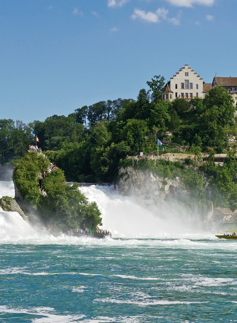 Rheinfall bei klarem Himmel und Schloss im Hintergrund.