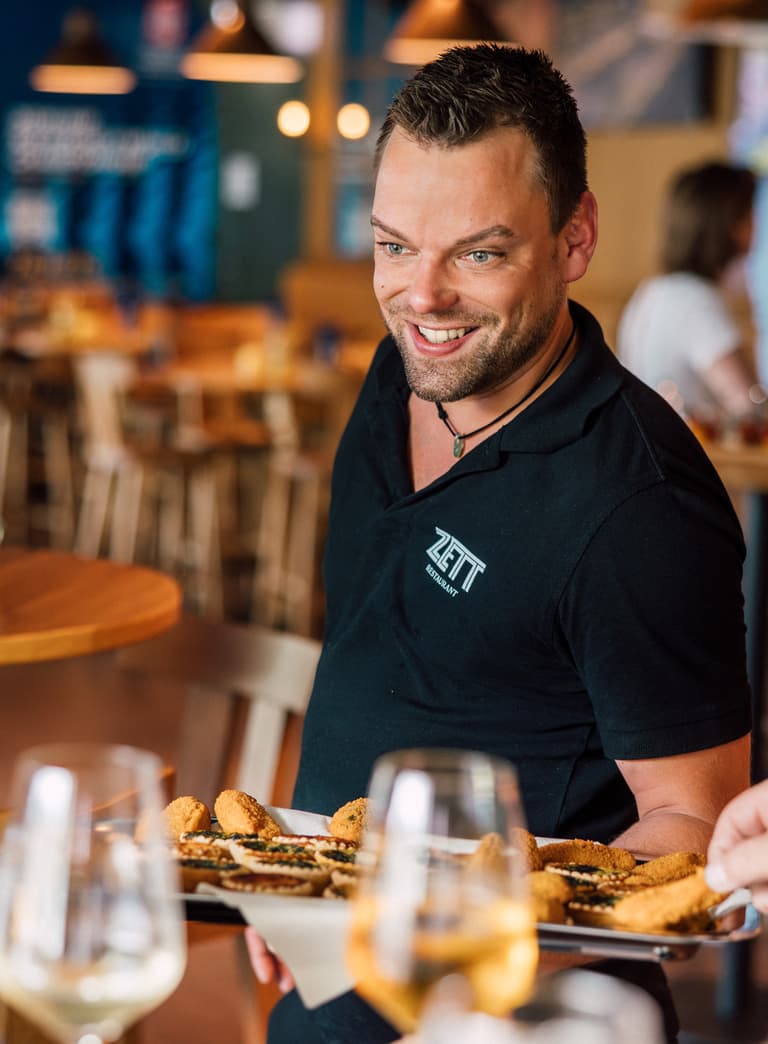 Kellner serviert Essen in einem Restaurant, lächelnd.