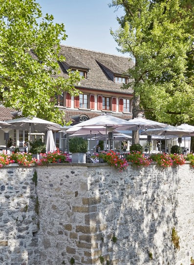Gemütliches Café mit Terrasse an Steinmauer mit Blumen und Bäumen.