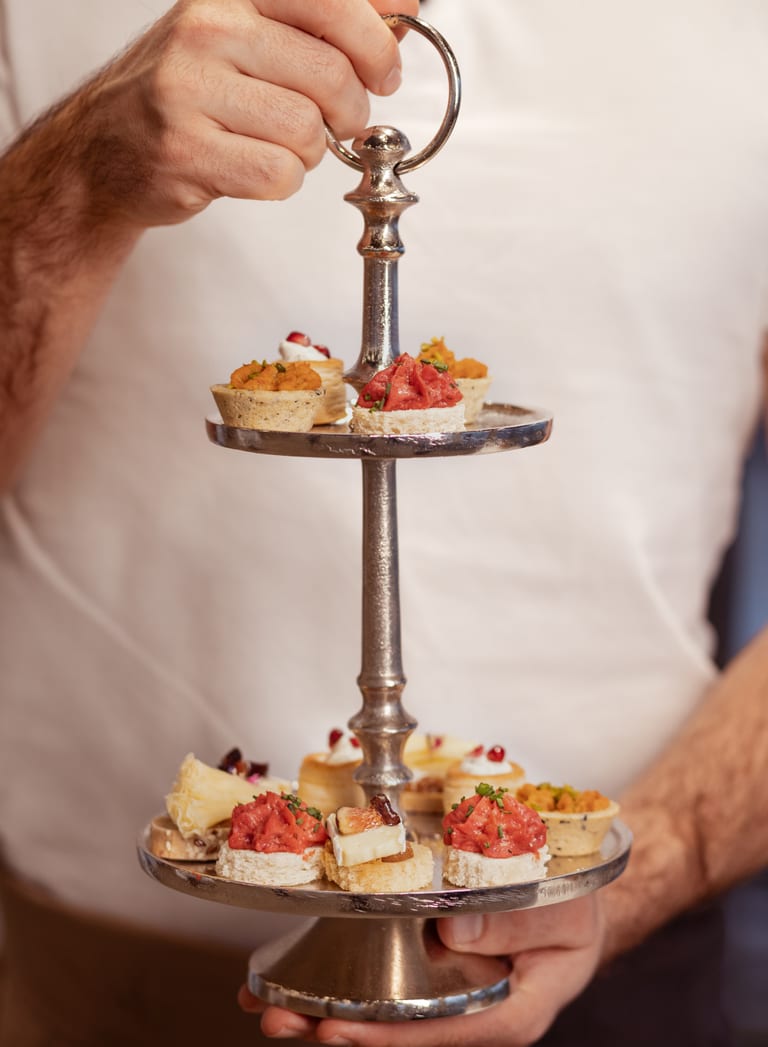 Person hält eine silberne Etagere mit kleinen Häppchen.