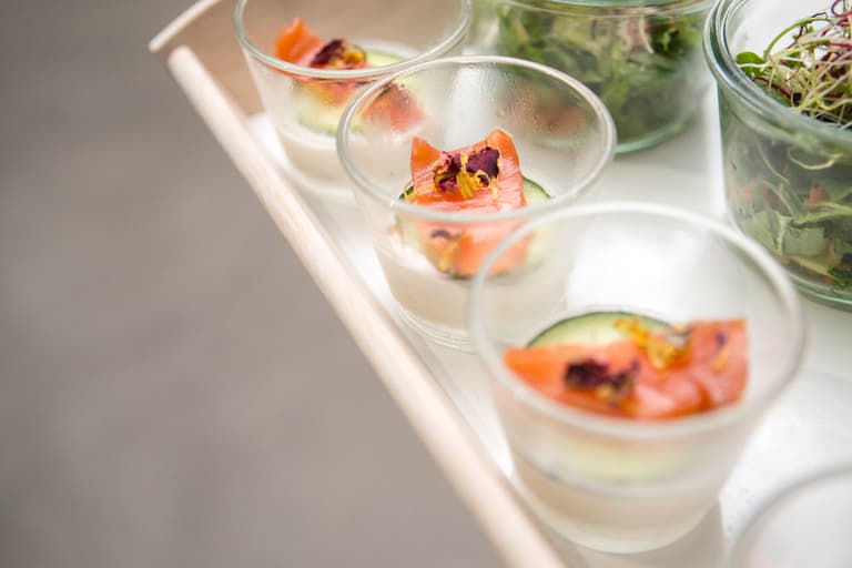Kleine Gläser mit Lachs und Gurkenscheiben auf Tablett.
