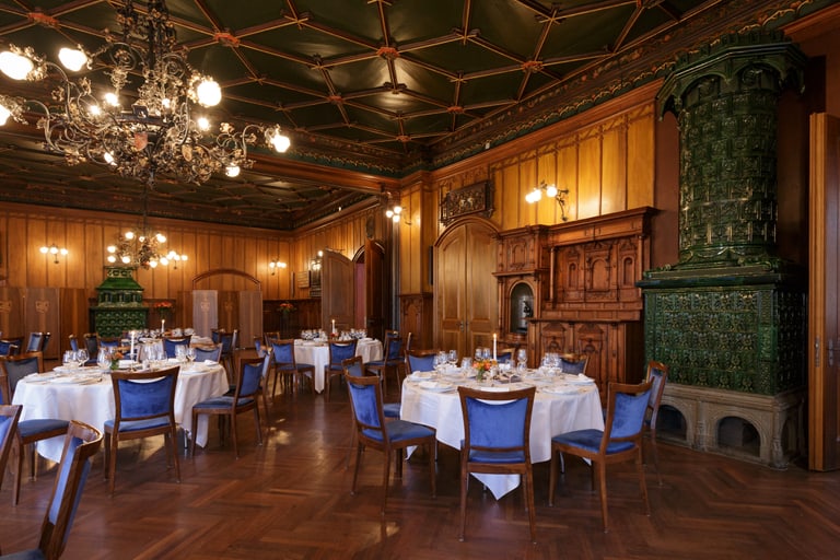 Elegantes Restaurant mit Holzmöbeln und runden Tischen, grüne Kachelofenwand.