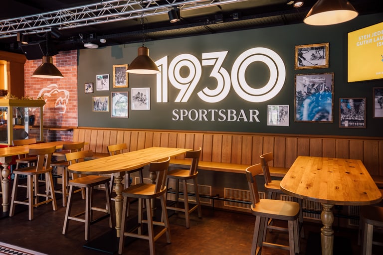Innenraum der 1930 Sportsbar mit Holztischen und dekorierten Wänden.
