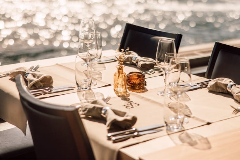Eleganter gedeckter Tisch mit Seeblick im Hintergrund.