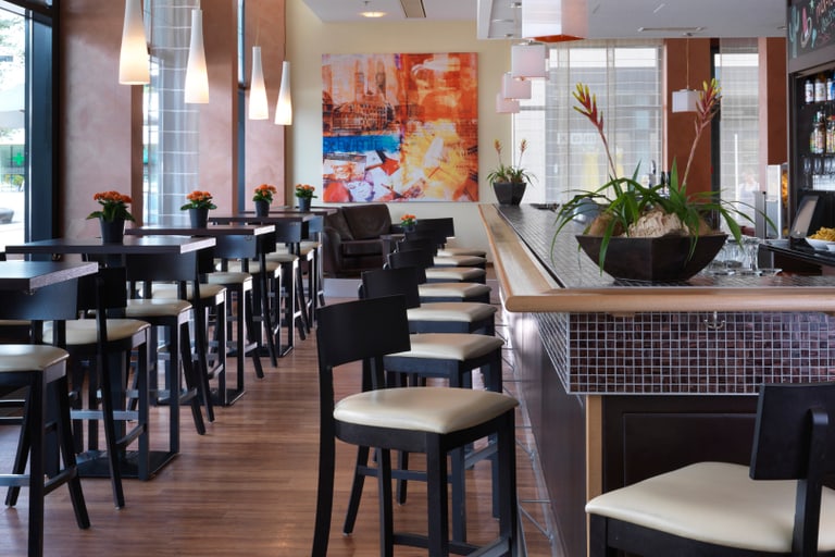 Moderne Bar mit hohen Tischen und Stühlen, Pflanzendekorationen.