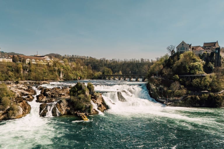 Rheinfall mit Schloss und Bäumen im Hintergrund.