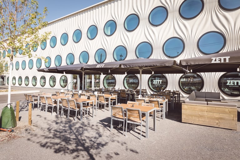 Aussenbereich eines Cafés mit runden Fenstern an der modernen Fassade.