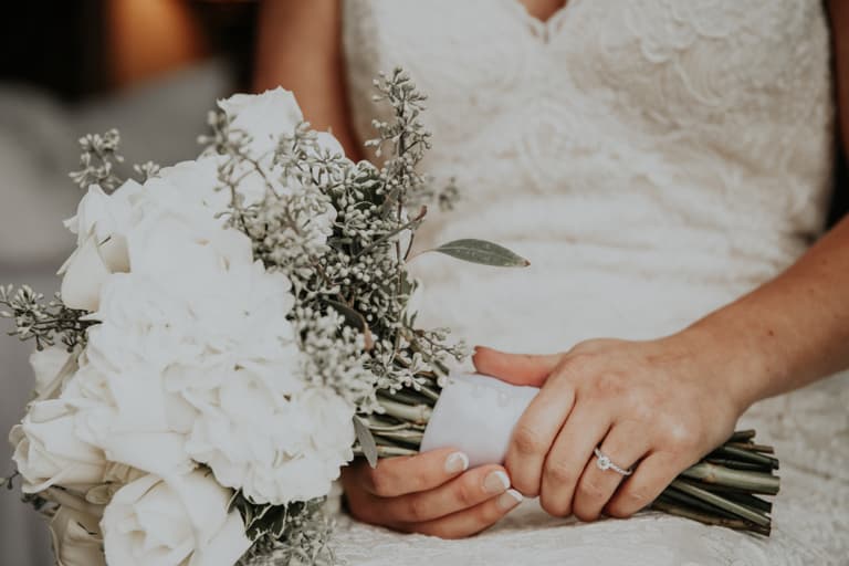 Braut mit Blumenstrauss in der Hand, Nahaufnahme des Kleides und Rings.