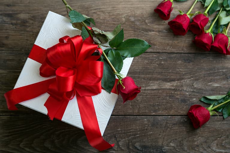 Geschenkbox mit roter Schleife und Rosen auf Holztisch.