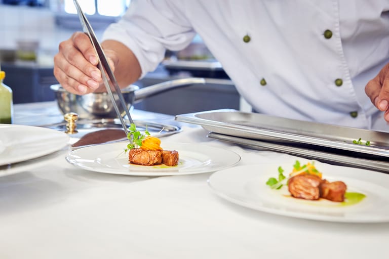 Koch arrangiert Gourmetgericht auf Teller in Küche.