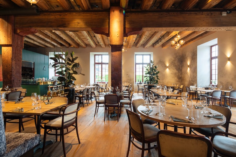 Elegantes Restaurant mit Holzbalkendecke und runden Tischen.