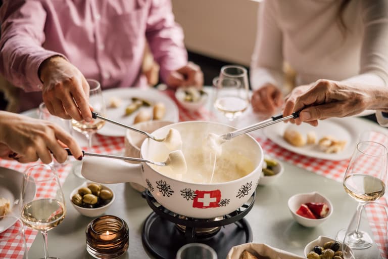 Menschen geniessen Käsefondue an einem Tisch mit Rotweingläsern.