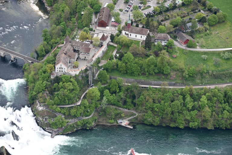 Luftbild des Rheinfalls mit Schloss Laufen und Gebäuden in grüner Landschaft.