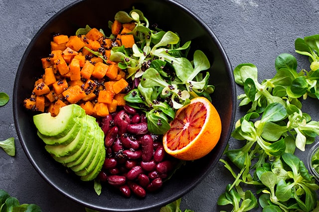 Schüssel mit Gemüse, roten Bohnen und halber Orange auf grauem Hintergrund.