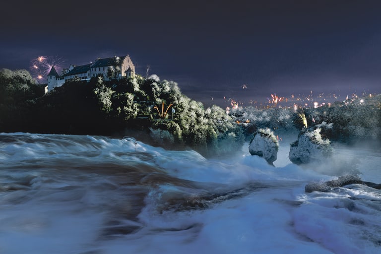 Schloss auf Hügel bei Nacht mit Fluss im Vordergrund und Feuerwerk am Himmel.