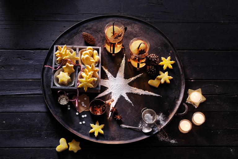 Dekorierte Tafel mit Weihnachtsplätzchen und Kerzen auf dunkelbraunem Hintergrund.