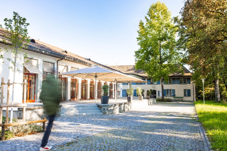 Person walking past a sunny building with a terrace.
