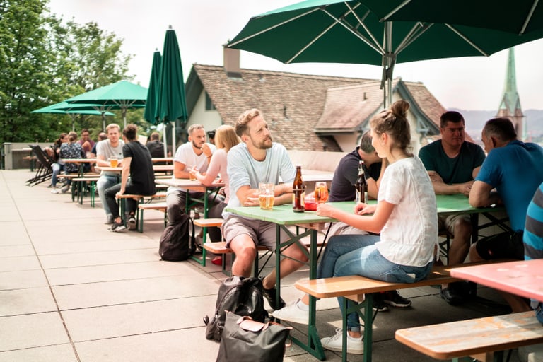 Menschen sitzen an Tischen im Freien mit Sonnenschirmen.",