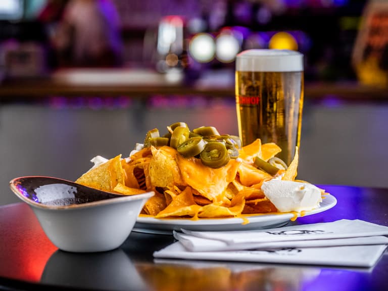 Nachos mit Jalapeños und Bier auf einem Tisch in einer Bar.
