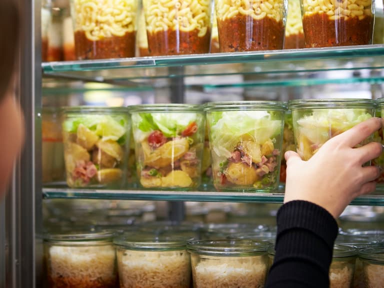 Person wählt ein Glas mit Salat aus Kühlschrank aus.