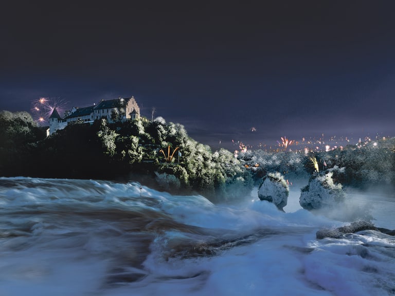 Wasserfall bei Nacht mit Schloss und Feuerwerk im Hintergrund.