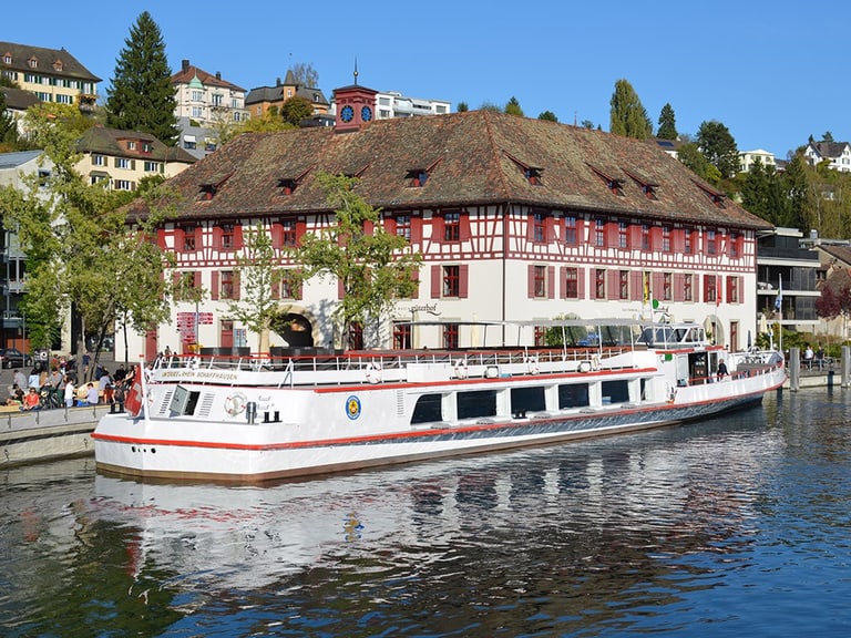 Weisses Boot an der Anlegestelle vor historischem Gebäude am Wasser.