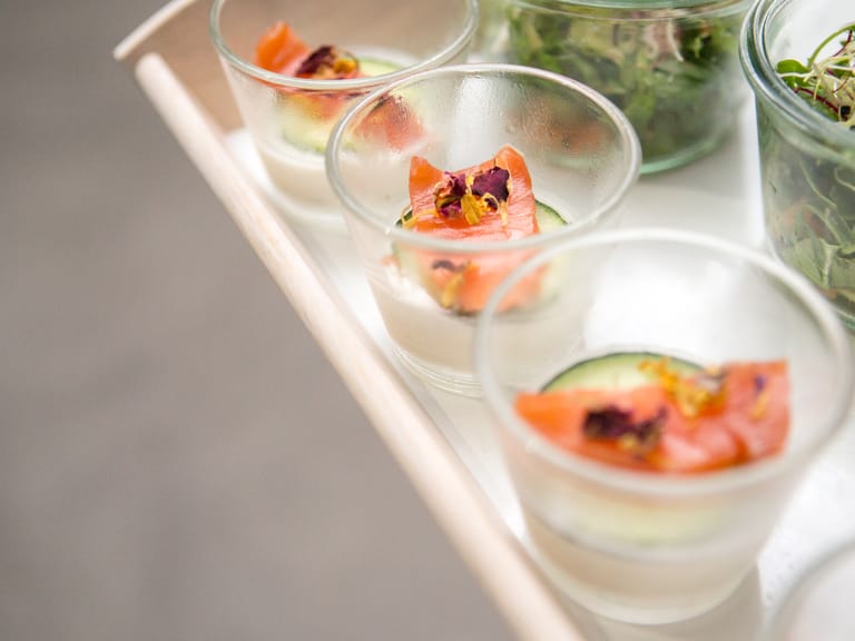 Kleine Gläser mit Lachs und Gurkenscheiben auf Tablett.