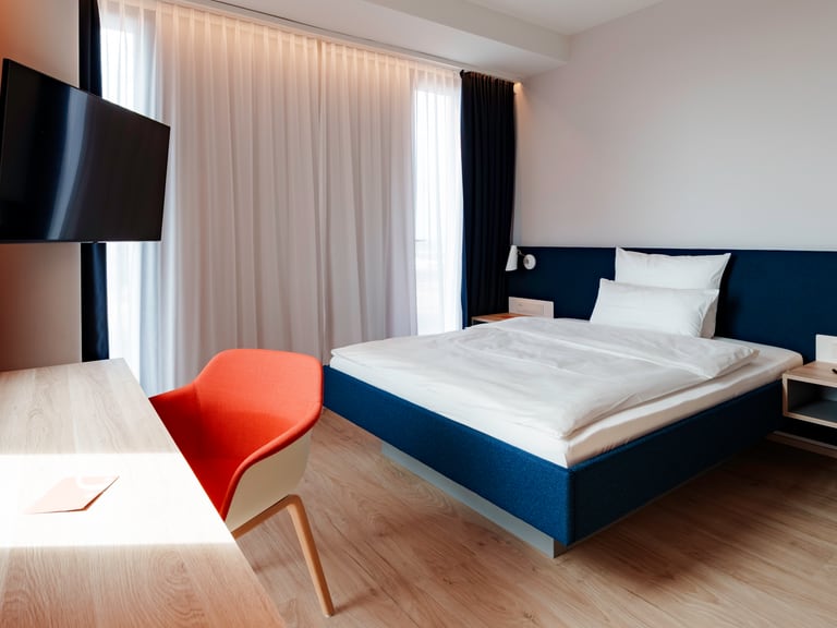 Modernes Hotelzimmer mit Bett, Tisch, Stuhl und Fernseher.