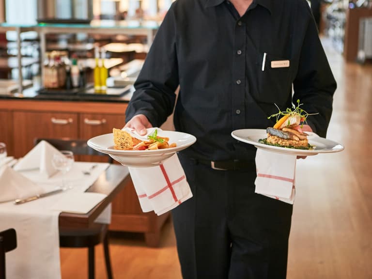 Kellner serviert zwei Teller mit Speisen im Restaurant.