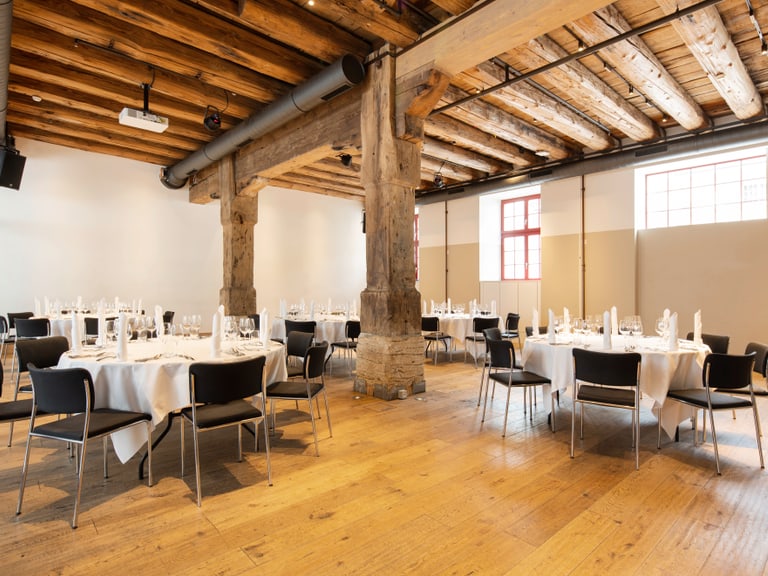 Eleganter Veranstaltungsraum mit gedeckten Tischen und Holzbalkendecke.