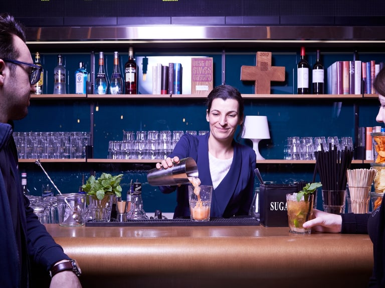 Barkeeper mixt Getränke für zwei Gäste am Tresen.