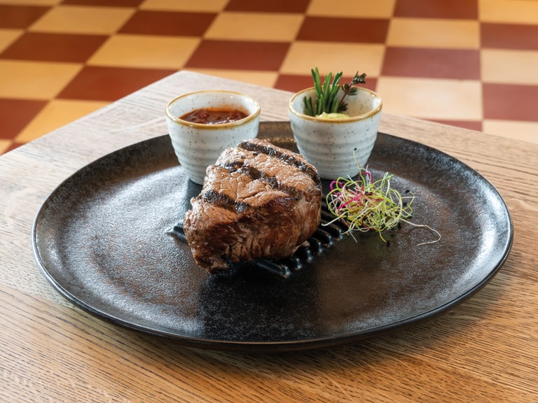 Gegrilltes Steak auf schwarzem Teller mit zwei Saucenschalen.