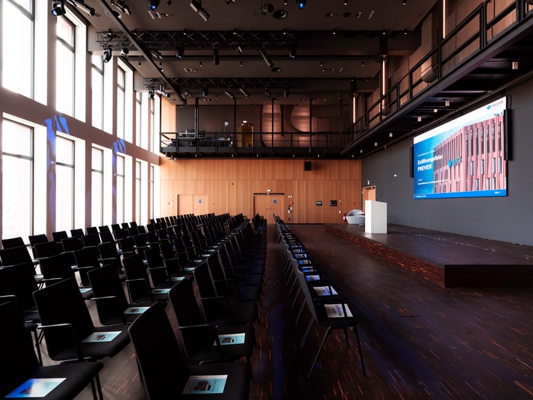 Leerer Konferenzraum mit Reihen von Stühlen und einer grossen Leinwand.