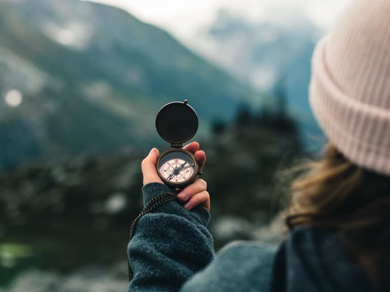 Person hält Kompass in Berglandschaft.