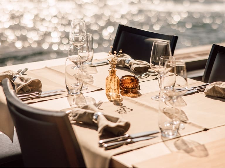 Eleganter gedeckter Tisch mit Seeblick im Hintergrund.