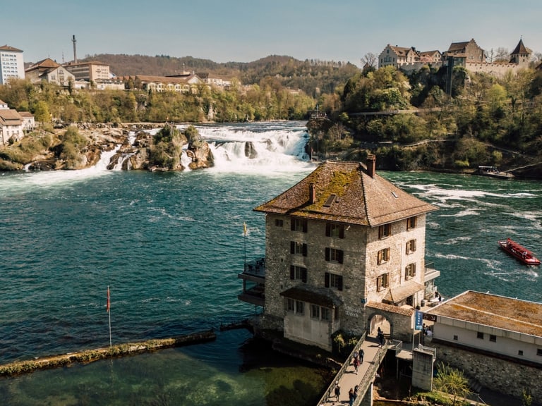 Luftbild der Rheinfall-Wasserfälle und umliegende Gebäude bei Sonnenschein.