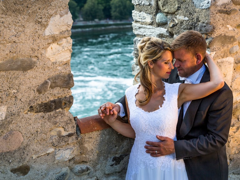 Brautpaar an steinerner Wand mit Fluss im Hintergrund.