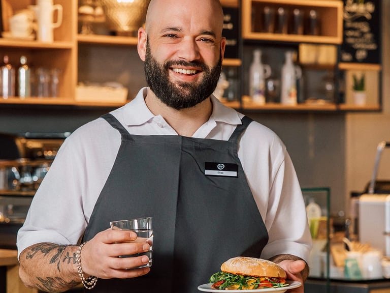 Mann im Café hält Glas Wasser und Teller mit Sandwich.