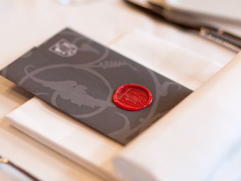 Schwarzer Umschlag mit rotem Wachssiegel auf Tischdecke.