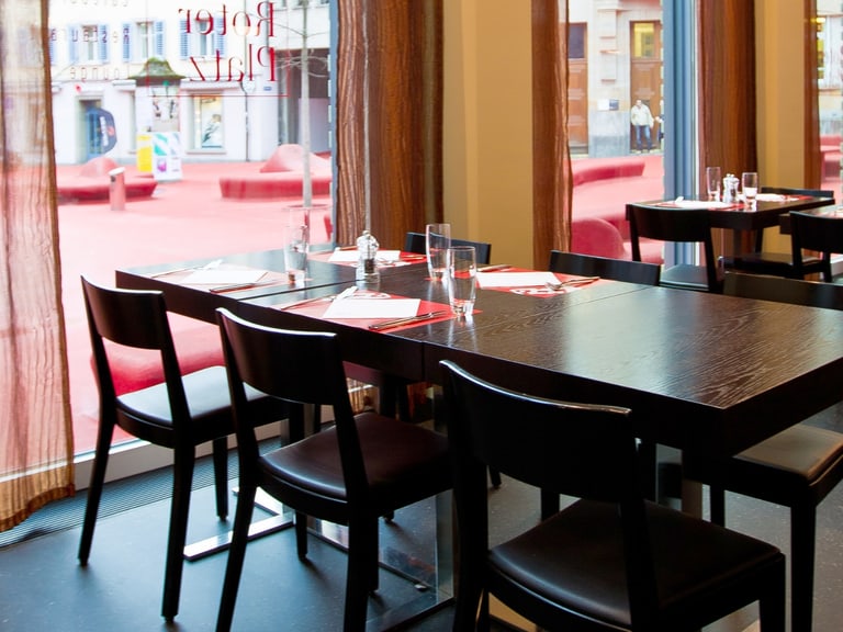 Leeres Restaurant mit gedeckten Tischen und grossen Fenstern.