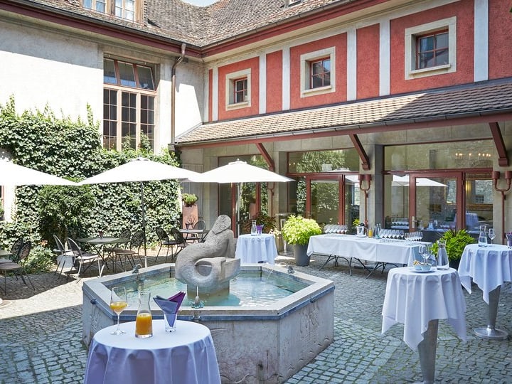 Innenhof mit Springbrunnen, Tischen und Sonnenschirmen.