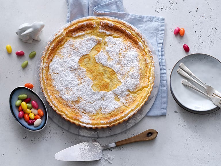 Zitronenkuchen mit Hasenmotiv, Ostereiern und Geschirr auf Tisch.